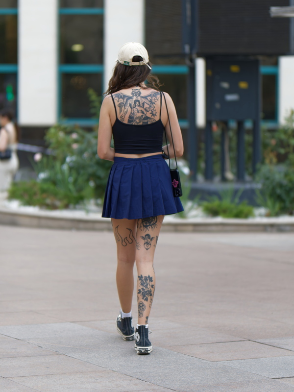 Girl wearing a summer streetwear outfit with an edgy, alternative aesthetic combining a classic navy pleated mini skirt with a simple cropped black cami top